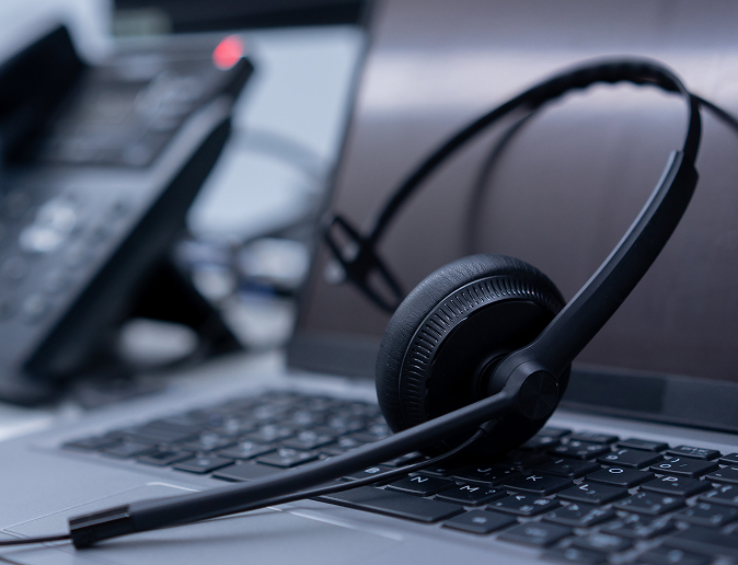 Čierny headset s mikrofónom položený na klávesnici notebooku, v pozadí kancelársky IP telefón – symbol moderného zákazníckeho servisu a efektívnej komunikácie na diaľku.